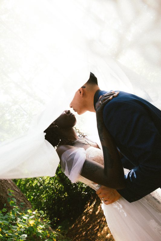 Groom kissing the bride under her veil in dappled light