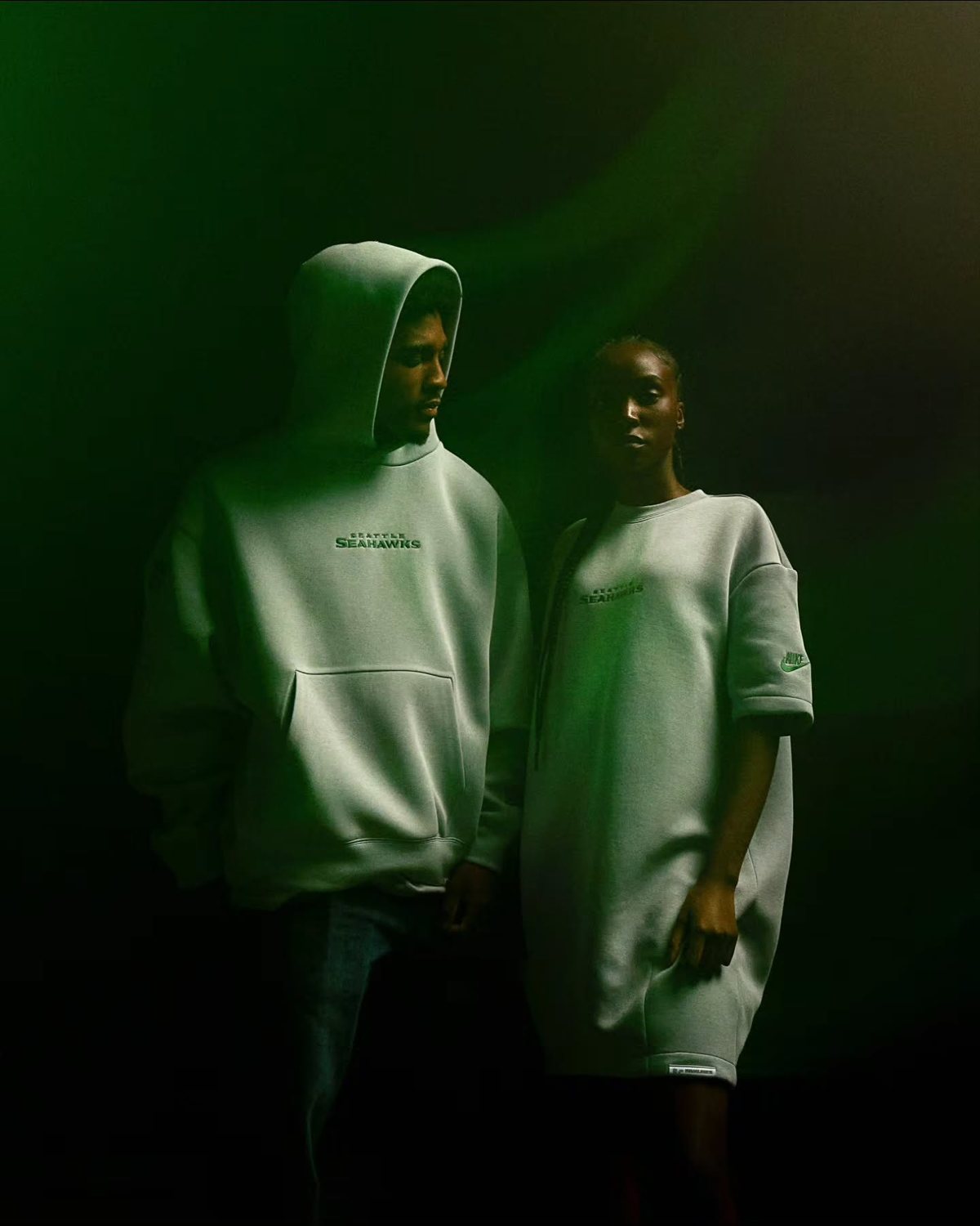 Two models in hoodies lit with green light