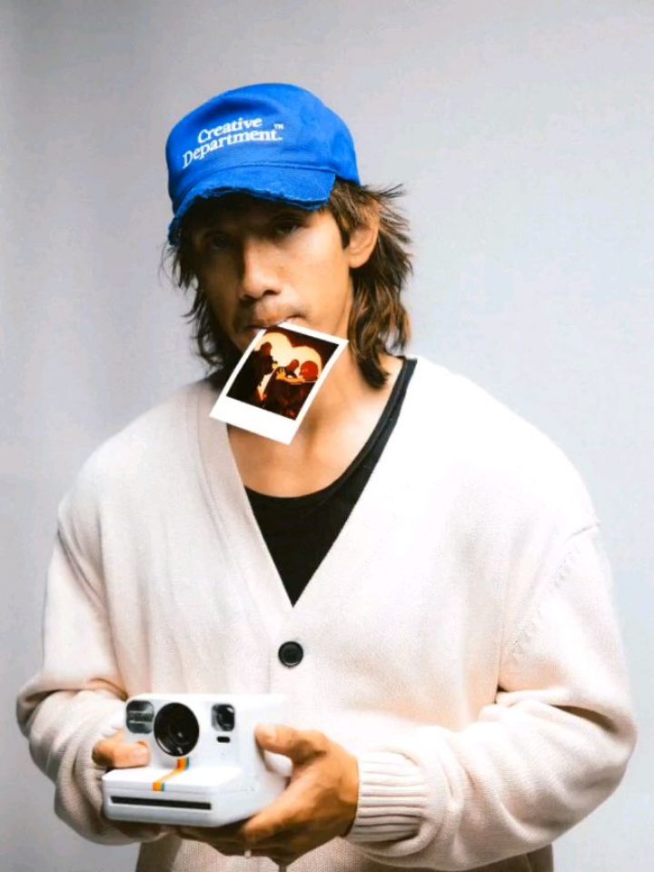 Nick Sisaiyaket in a blue cap, a Polaroid in his mouth, holding an instant camera