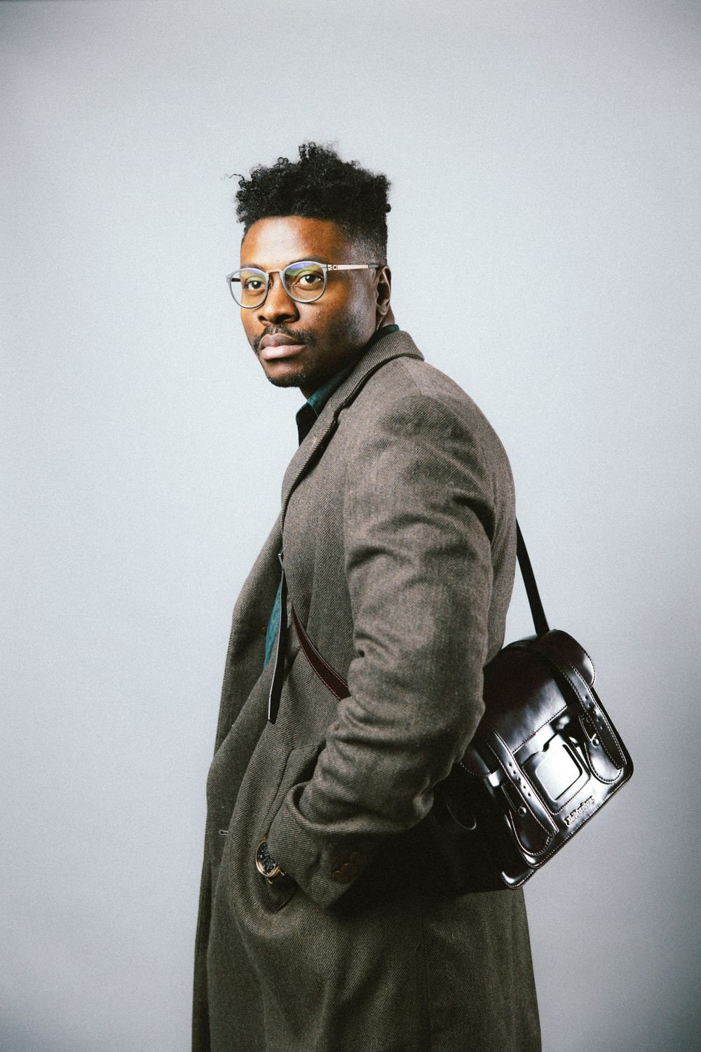 Man in a long coat with a leather bag on a white backdrop